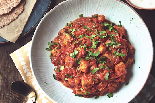 A curry made with Quorn Pieces and tomato garnished with coriander in a white bowl.