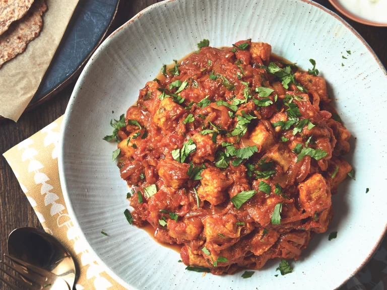 A curry made with Quorn Pieces and tomato garnished with coriander in a white bowl.