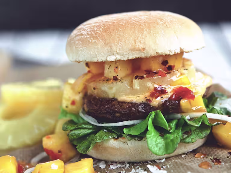 Veggie burger recipe made with Quorn Quarter Pounders on top of lettuce garnished with onions, pineapple and mango salsa in a bun