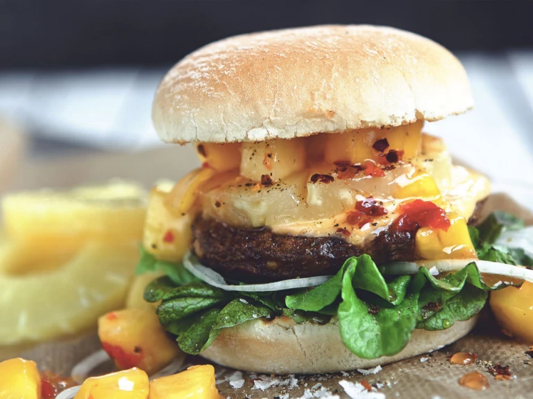 Veggie burger recipe made with Quorn Quarter Pounders on top of lettuce garnished with onions, pineapple and mango salsa in a bun