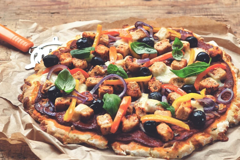 A meat free pizza topped with Quorn pieces resting on baking paper with a pizza cutter beside the pizza.