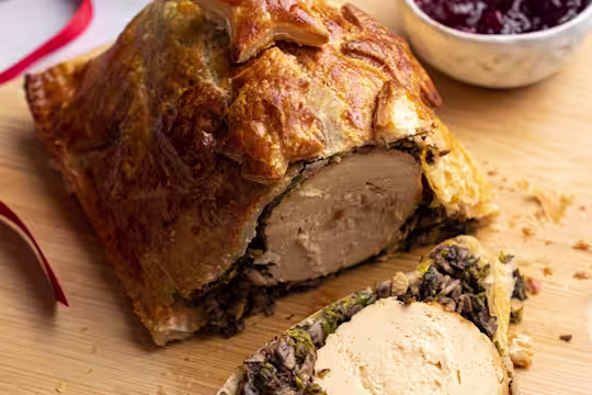 Quorn Vegetarian Roast Christmas Wellington on a board with a side of cranberry sauce.