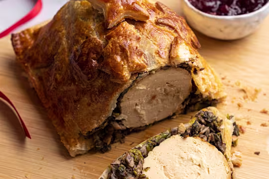 Quorn Vegetarian Roast Christmas Wellington on a board with a side of cranberry sauce.