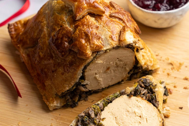 Quorn Vegetarian Roast Christmas Wellington on a board with a side of cranberry sauce. 