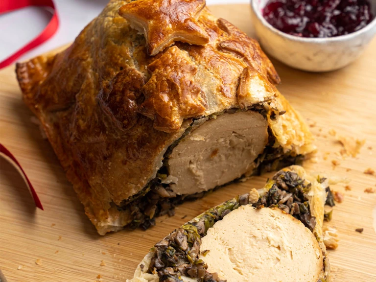 Quorn Vegetarian Roast Christmas Wellington on a board with a side of cranberry sauce. 