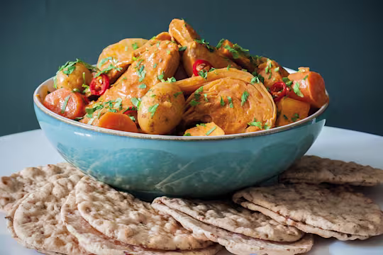 A blue bowl of Senegalese mafe made with Quorn Vegetarian Fillets and vegetables with small flatbreads on the side.
