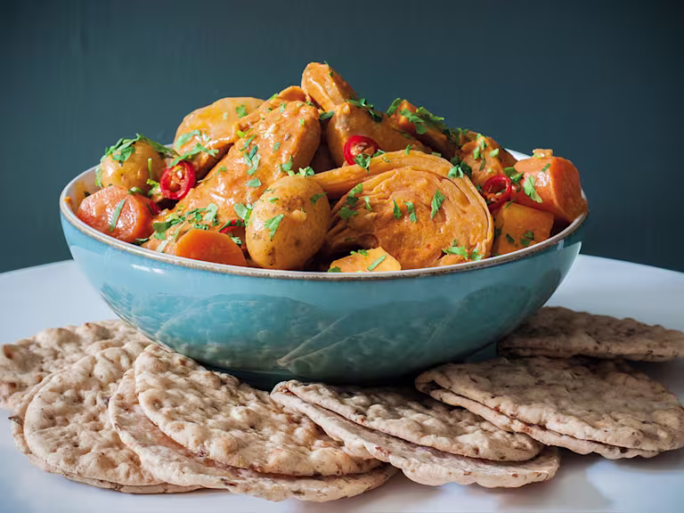 A blue bowl of Senegalese mafe made with Quorn Vegetarian Fillets and vegetables with small flatbreads on the side.