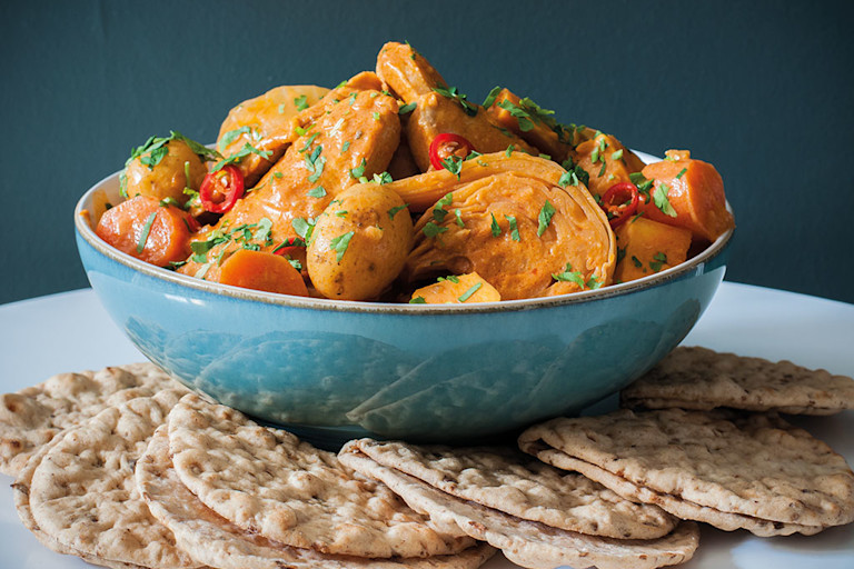 A blue bowl of Senegalese mafe made with Quorn Vegan Pieces and vegetables with small flatbreads on the side.