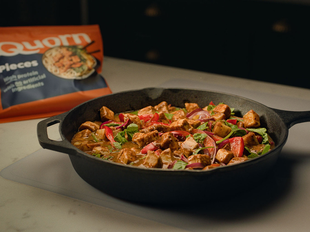 Quorn Pieces in a Massaman curry sauce with chopped peppers and onion served with white rice in a black bowl with lime garnish.