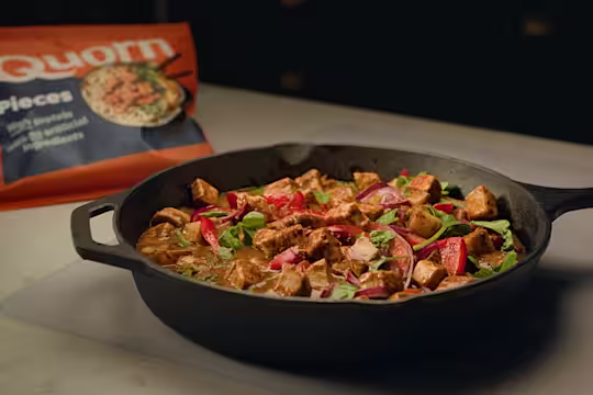 Quorn Pieces in a Massaman curry sauce with chopped peppers and onion served with white rice in a black bowl with lime garnish.