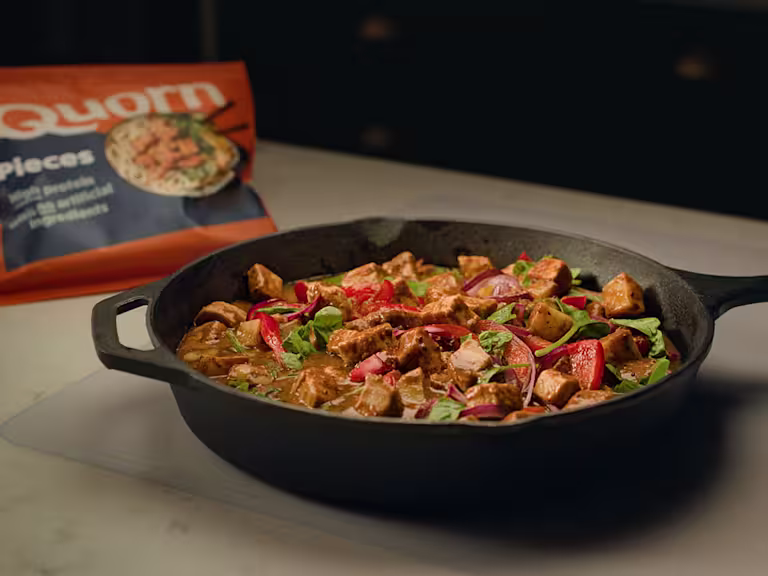 Quorn Pieces in a Massaman curry sauce with chopped peppers and onion served with white rice in a black bowl with lime garnish.