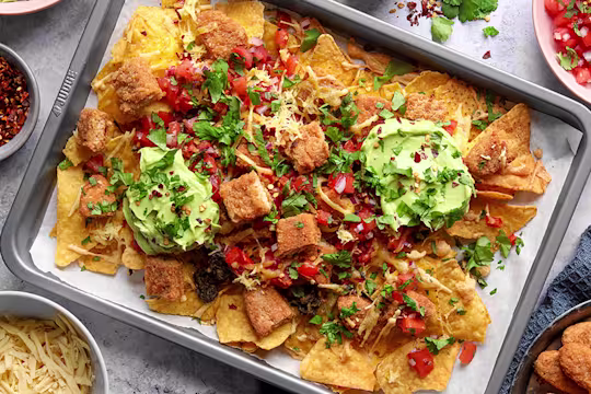 A grey baking sheet with tortilla chips, guacamole, salsa, chopped up Quorn Salt and Pepper Tenders and cheese with a herb garnish.