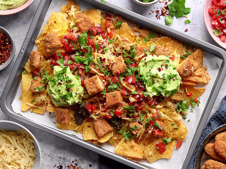 A grey baking sheet with tortilla chips, guacamole, salsa, chopped up Quorn Salt and Pepper Tenders and cheese with a herb garnish.