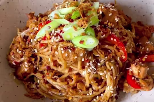 Sweet chilli noodles with Quorn Vegetarian Chicken pieces, red pepper, onions and beansprouts in a bowl garnished with spring onion and sesame seeds.