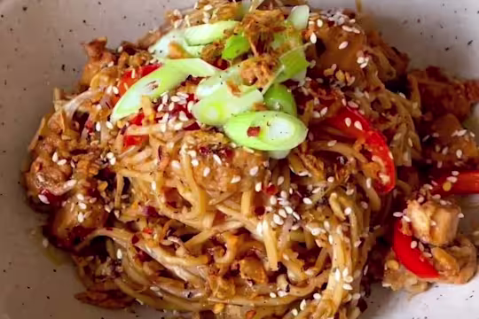 Sweet chilli noodles with Quorn Vegetarian Chicken pieces, red pepper, onions and beansprouts in a bowl garnished with spring onion and sesame seeds.