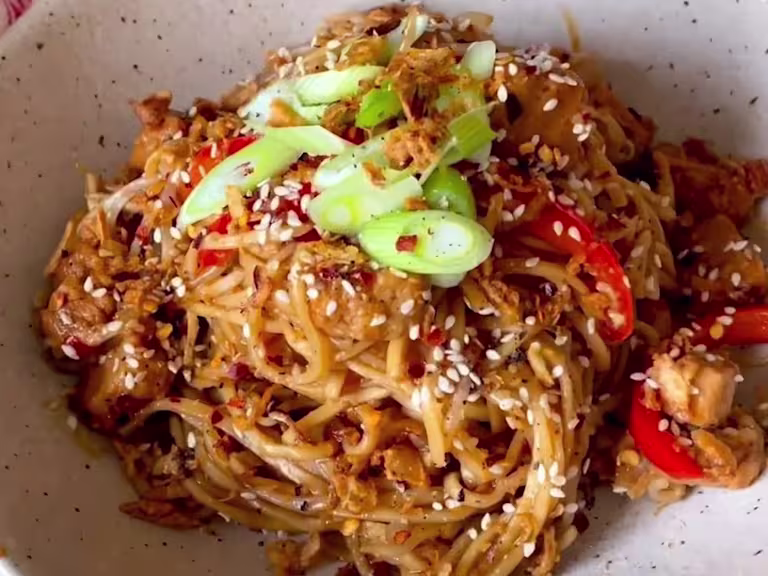 Sweet chilli noodles with Quorn Vegetarian Chicken pieces, red pepper, onions and beansprouts in a bowl garnished with spring onion and sesame seeds.