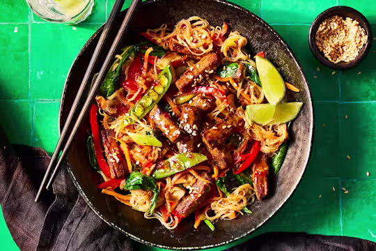 A vibrant plate of Korean japchae with Quorn Steak Strips featuring colorful vegetables and noodles, garnished with lime and sesame seeds