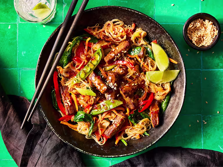 A vibrant plate of Korean japchae with Quorn Steak Strips featuring colorful vegetables and noodles, garnished with lime and sesame seeds