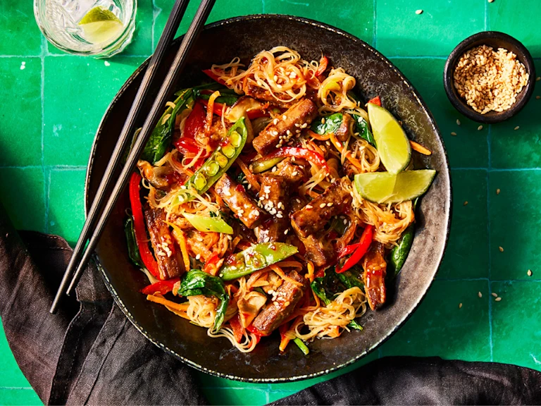 A vibrant plate of Korean japchae with Quorn Steak Strips featuring colorful vegetables and noodles, garnished with lime and sesame seeds