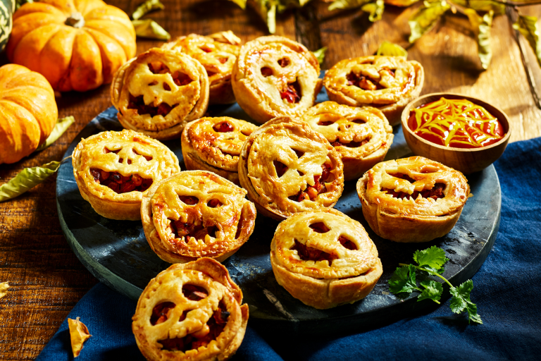 A tray full of mini pies filled with diced Quorn Cocktail Sausages topped with pastry carved like jack-o-lanterns.