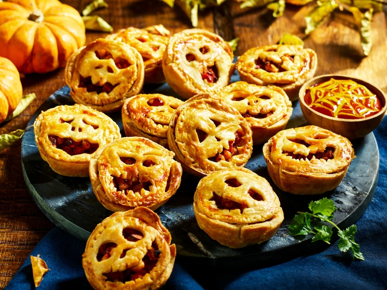 A tray full of mini pies filled with diced Quorn Cocktail Sausages topped with pastry carved like jack-o-lanterns.