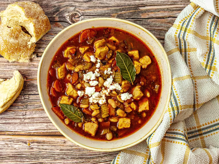 Greek fasolada served in a bowl with crusty bread and garnished with feta cheese
