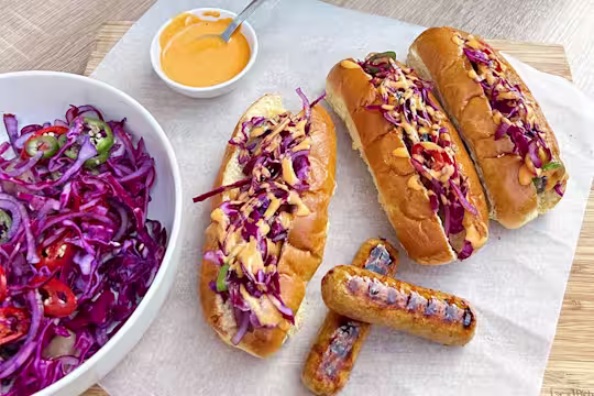 Three sticky Asian-style vegetarian hot dogs with a side of slaw and two Quorn Sausages on display.