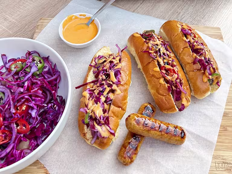 Three sticky Asian-style vegetarian hot dogs with a side of slaw and two Quorn Sausages on display.