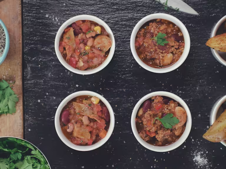 Chilli con carne made with Quorn Vegetarian Shredded Steak served in 4 ramekins next to potato wedges on a black slate