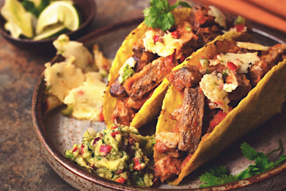 Two hard shell tacos filled with Quorn Meatless Steak-style Strips, cheese, and salsa, with guacamole and queso fundido on the side.