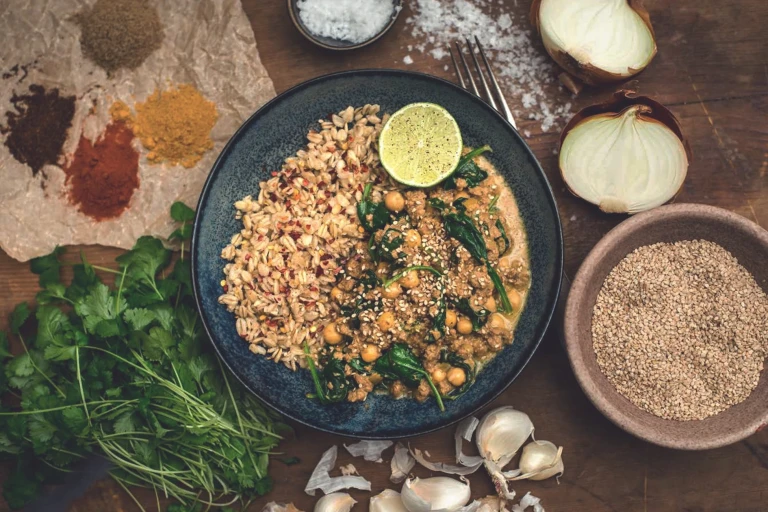 A chickpea and spinach curry made with Quorn Mince topped with sesame seeds and served with a side of cooked oats and a wedge of lime.