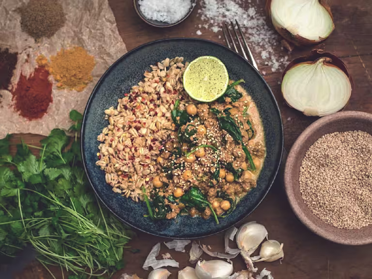 A chickpea and spinach curry made with Quorn Grounds topped with sesame seeds and served with a side of cooked oats and a wedge of lime.