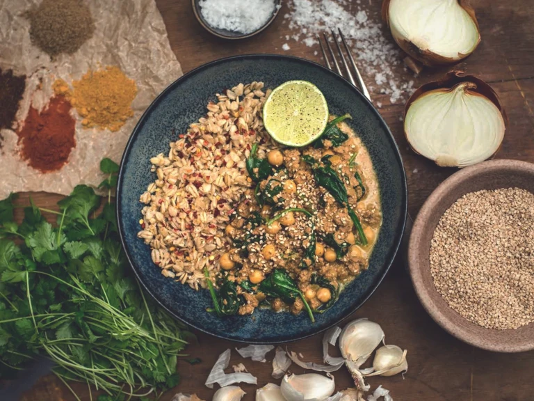 A chickpea and spinach curry made with Quorn Mince topped with sesame seeds and served with a side of cooked oats and a wedge of lime.