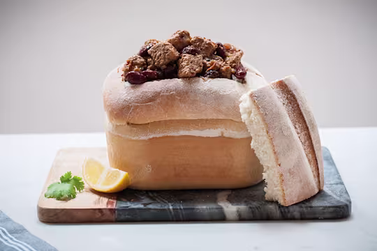 A hollowed-out loaf of bread filled with Bunny Chow made with Quorn Pieces with a wedge of lemon on the side.