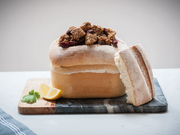 A hollowed-out loaf of bread filled with Bunny Chow made with Quorn Pieces with a wedge of lemon on the side.