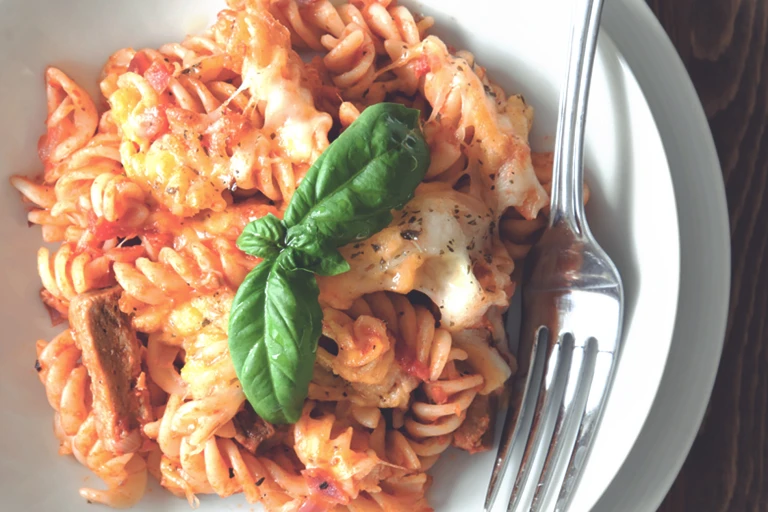 A plate of vegetarian pasta bake made with Quorn Vegetarian Steak Strips, fusilli pasta, and tomato sauce, topped with plenty of cheese and a sprig of basil.