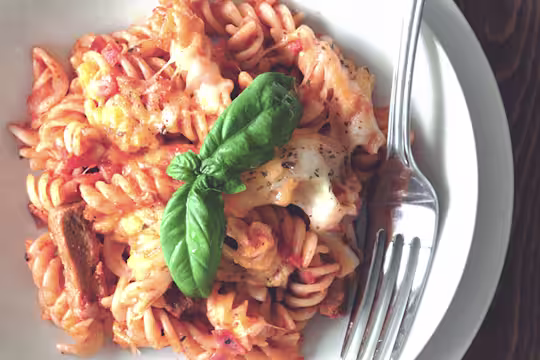 A plate of vegetarian pasta bake made with Quorn Vegetarian Steak Strips, fusilli pasta, and tomato sauce, topped with plenty of cheese and a sprig of basil.