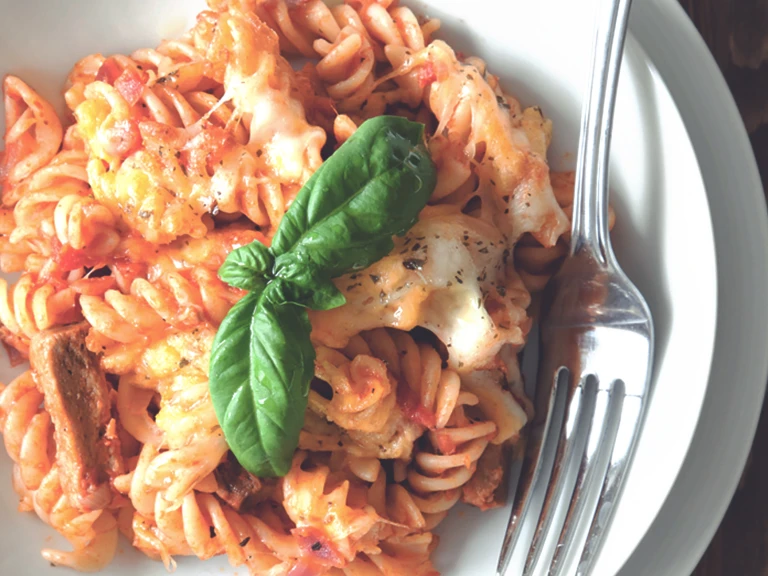 A plate of vegetarian pasta bake made with Quorn Vegetarian Steak Strips, fusilli pasta, and tomato sauce, topped with plenty of cheese and a sprig of basil.