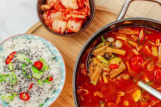 Korean Doenjang Jigae using Quorn Steak Strips in a bowl with a bowl of rice on the side.