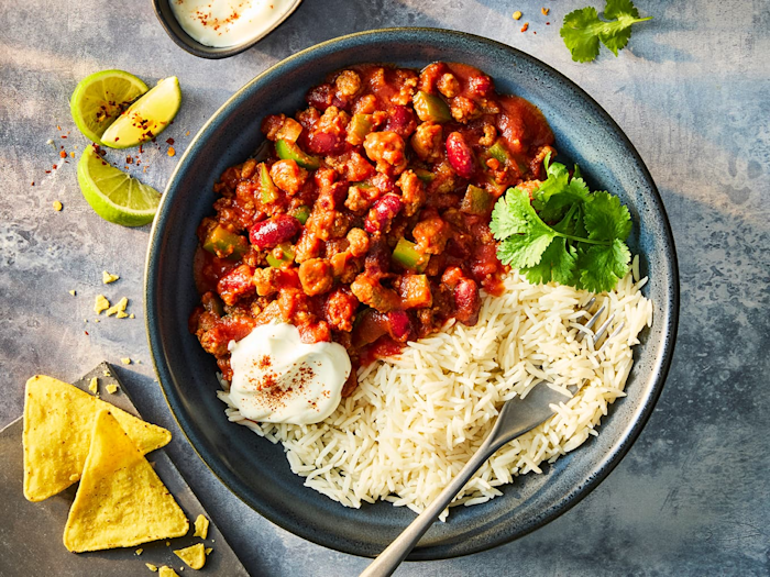 Quorn slow cooker chilli with Quorn Mince in a blue bowl served with white rice, sour cream and tortilla chips.