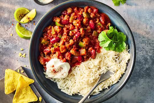 Quorn slow cooker chilli with Quorn Mince in a blue bowl served with white rice, sour cream and tortilla chips.