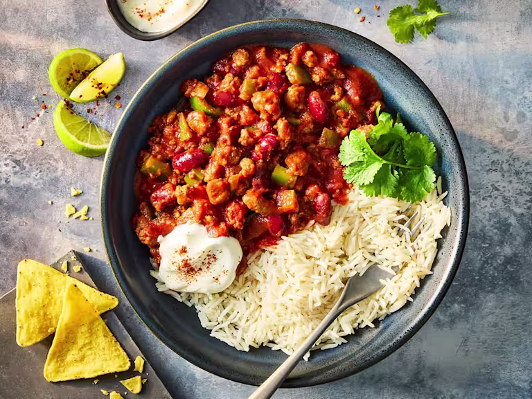 Quorn slow cooker chilli with Quorn Mince in a blue bowl served with white rice, sour cream and tortilla chips.