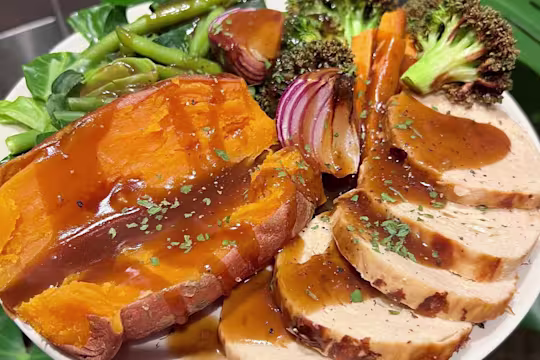 Quorn Roast on a plate served with sweet potato and roasted vegetables such as broccoli, onion, carrot and green beans, drizzled in gravy.