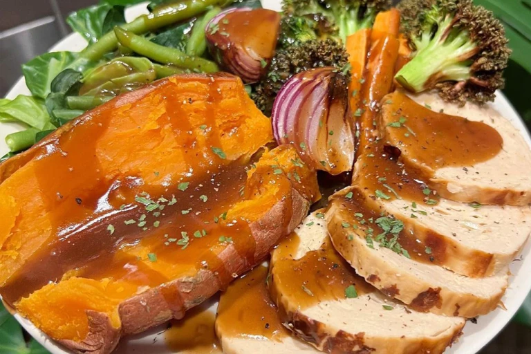 Quorn Roast on a plate served with sweet potato and roasted vegetables such as broccoli, onion, carrot and green beans, drizzled in gravy. 