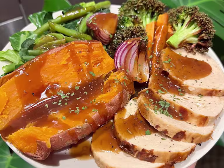 Quorn Roast on a plate served with sweet potato and roasted vegetables such as broccoli, onion, carrot and green beans, drizzled in gravy.