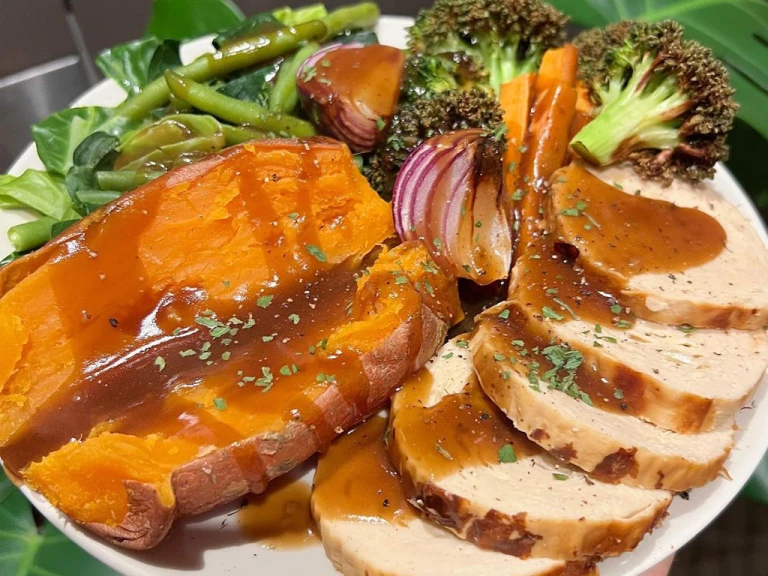 Quorn Roast on a plate served with sweet potato and roasted vegetables such as broccoli, onion, carrot and green beans, drizzled in gravy. 