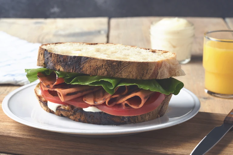 A BLT sandwich on rustic white bread with mayonnaise, lettuce, sliced tomatoes, and grilled Quorn Vegetarian Bacon Slices.