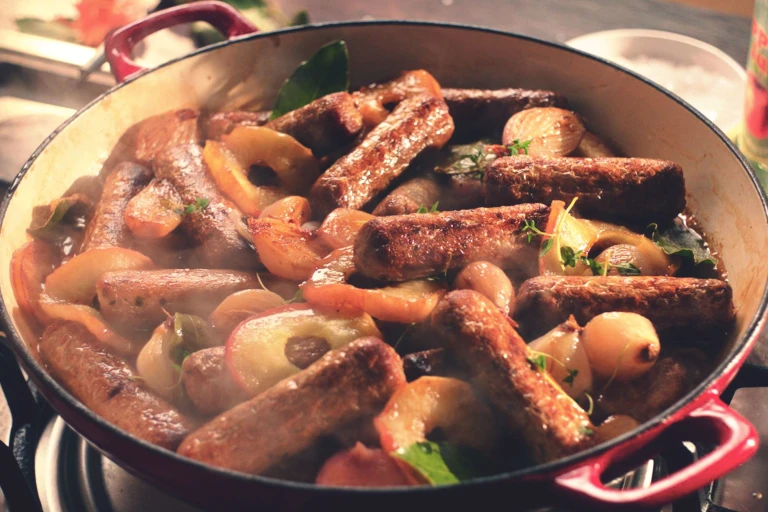 A casserole made with Quorn Sausages, shallots, and apples in a shallow Dutch oven.