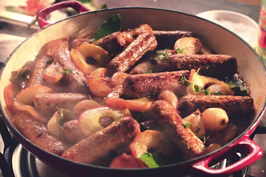 A casserole made with Quorn Sausages, shallots, and apples in a shallow Dutch oven.