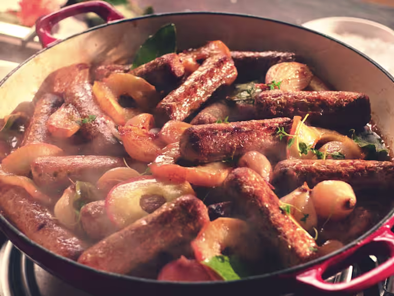 A casserole made with Quorn Sausages, shallots, and apples in a shallow Dutch oven.